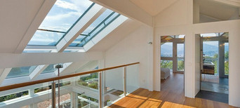 Modernes Dachgeschoss mit großen Glasdachfenstern, Holzfußboden und Glasgeländer, lichtdurchflutet mit Panoramablick.